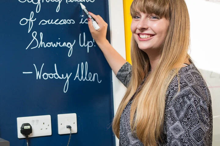 Woman writing on clear dry erase Paint blue office wall